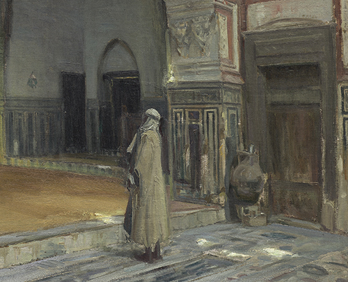 A man stands inside of a shadowy mosque and looks off at some point not shown.