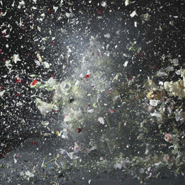 Still from video depicting an apple bursting into small fragments from gunshot