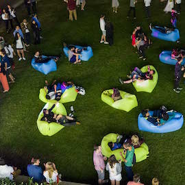 Visitors lounging on large neon-colored beanie bags spread out over courtyard grass 