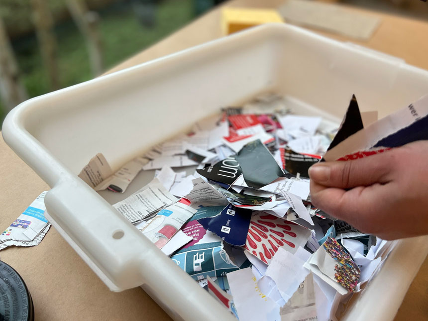 hand reaching into bin of paper pieces torn from magazines and newspapers