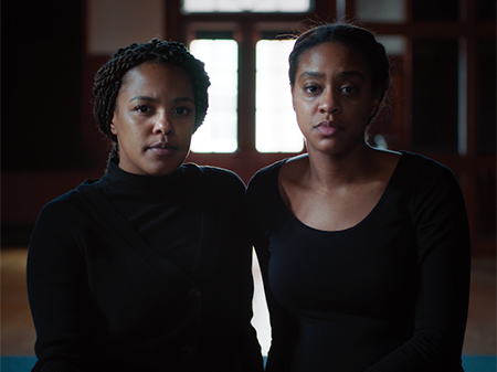 Two woman in black shirts stare directly ahead.