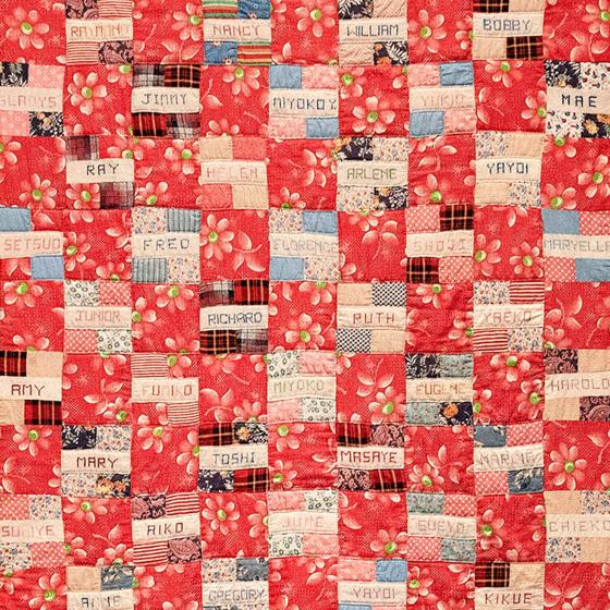 A quilt with red and white squares with names sewn onto them.