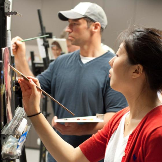 Two adult students paint on easels in classroom