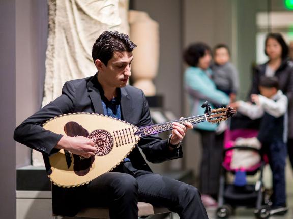 Lute player performing in Ancient Greece gallery, family with stroller watching in background