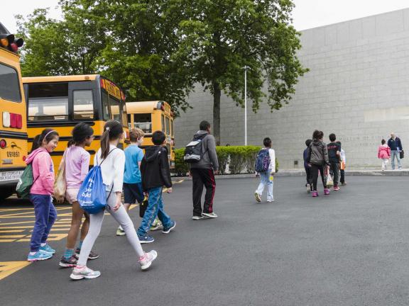 Line of students walking towards group entrance from parked buses