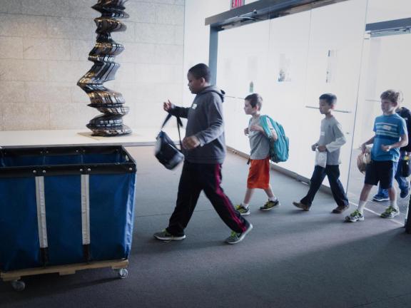 Student walking in through group entrance, about to drop off bag in bin
