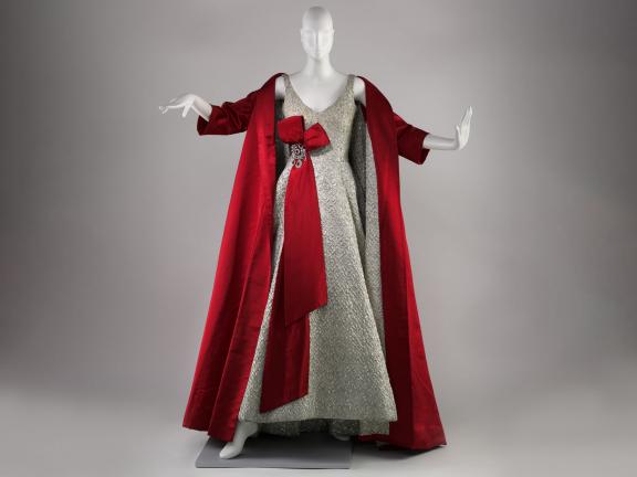 Mannequin wearing a silver floor length v-neck dress with red cape and red bow at waist