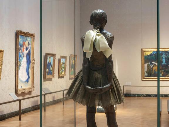 Degas sculpture of young dancer in foreground with impressionist paintings hanging on gallery walls in background