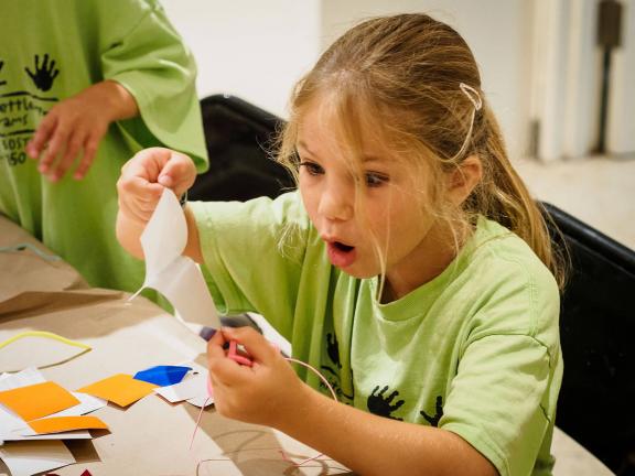 Young girl with expression of amazement while peeling a sticker to make artk.