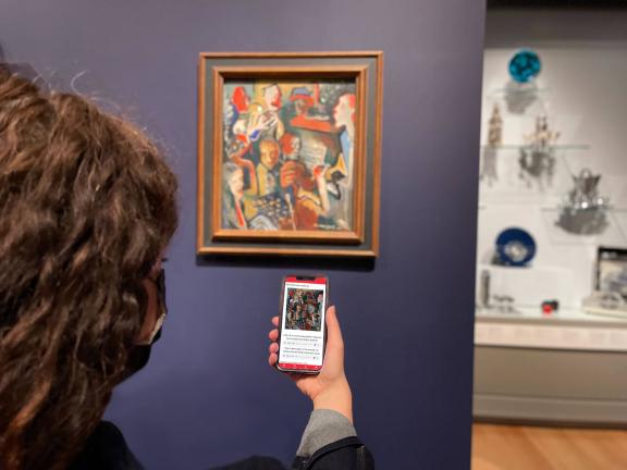 Visitor holding up smartphone with MFA Mobile tour on screen, in front of colorful, expressive painting depicting various musicians performing