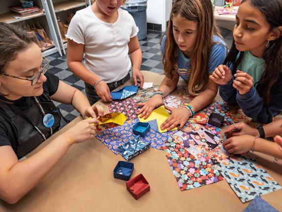 Instructor demonstrates origami with colorful paper while young students observe (SAC)