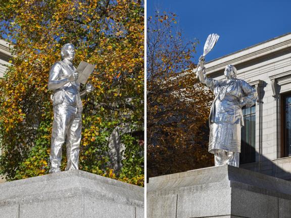 At left, a silver sculpture of Andre StrongBearHeart Gaines Jr. reading from piece of paper; at right, a silver sculpture of Julia Marden in traditional regalia holding up fan made of turkey feathers