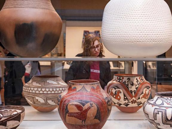 A woman looks at ceramic vessels through a glass case.