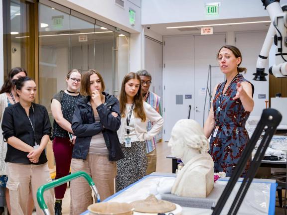 A group of college and university students listen to a presentation in front of a marble bust in the MFA's conservation workspaces
