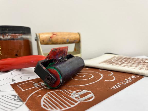 A close-up of a brayer, brown ink, and other printmaking supplies on a table