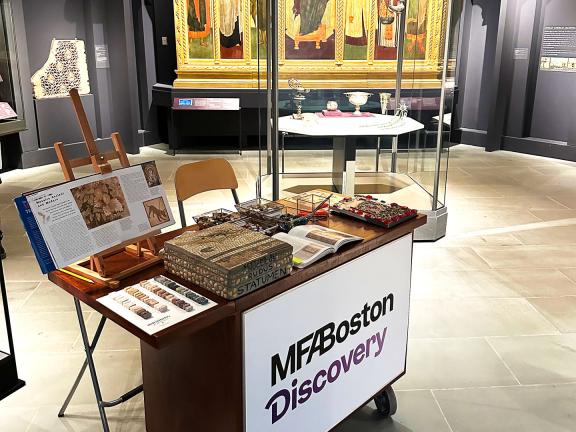 Sitting in a Museum gallery is a cart labeled "MFA Discovery" with various materials and art supplies on it