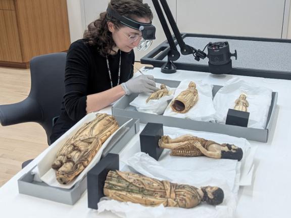 Conservator examining a group of six ivory figures lying horizontally on a table