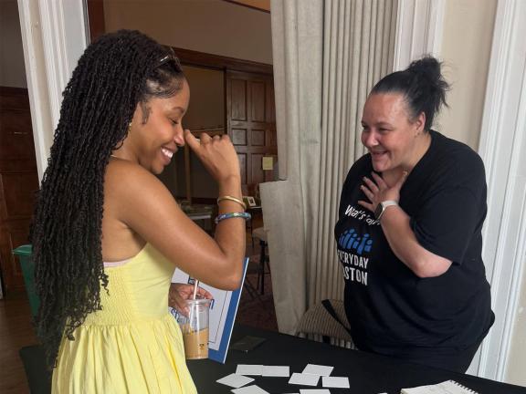A woman with an Everyday Boston t-shirt engages in lively conversation with a young woman in a yellow dress