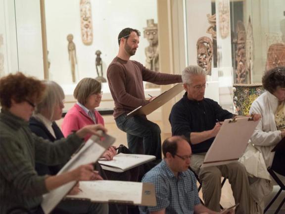 A group of people in an African art gallery sketch on large sketchbooks