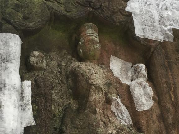 Detail of carved figures on a stone slab with areas of the stone covered by squares of a thin white tissue to prevent further flaking and loss