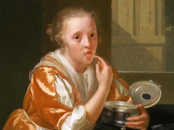 A young woman dressed in orange silks raises her finger to her mouth with a look of surprise on her face.
