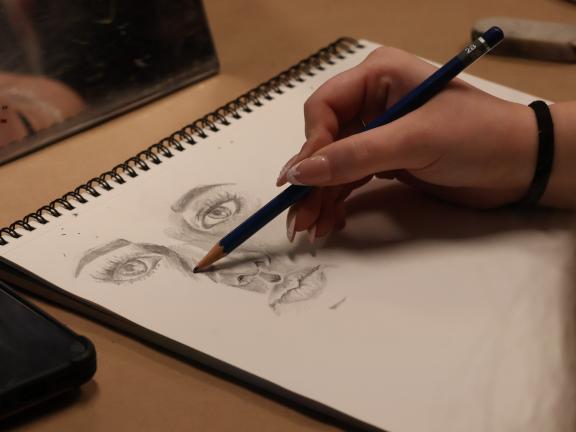 student draws face in sketchbook 