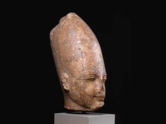 Ancient stone sculpture head of Amenhotep III with a tall headdress, exhibiting a serene expression