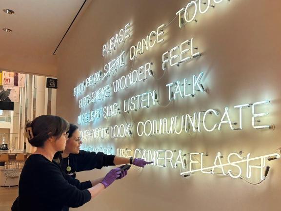 Two people adjust a neon sign on a wall