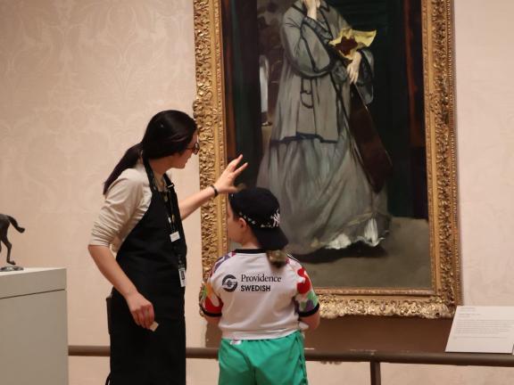 Studio Art Instructor in smock discusses painting in gallery with young student (SAC)