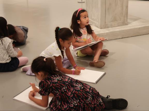Young students sit on gallery floor and draw from observation in sketchbooks (SAC)