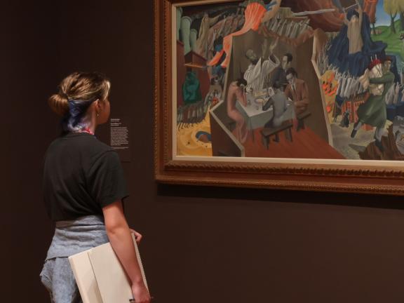 Teen student holding sketchbook examines artwork in gallery (SAC)