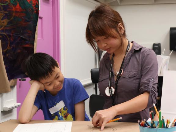 Studio Art teaching assistant draws with young boy in classroom (SAC)