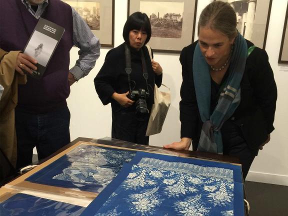 Three individuals closely examine blue textiles with intricate white patterns