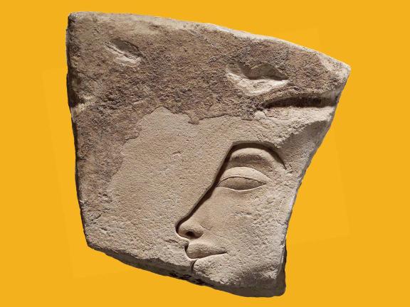 A weathered, uneven piece of limestone with a sunk relief profile of King Akhenaten's face