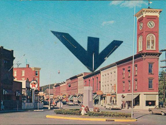 A vintage small-town street scene with a red brick clock tower, retro cars, and shops. 