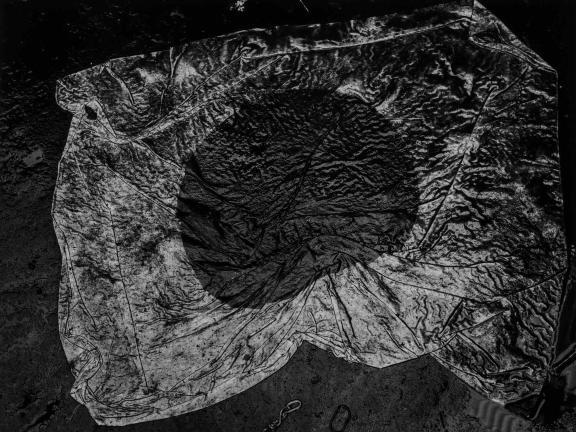 A weathered Japanese flag lies on a dark, textured surface. The fabric is wrinkled and stained