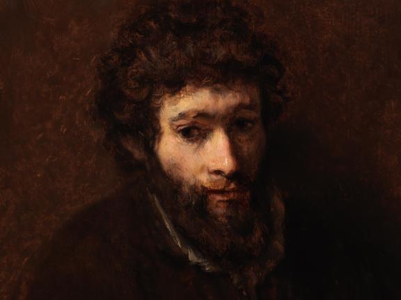 A young bearded man against a dark brown background.