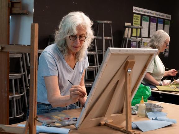 Adult female student paints on table top easel in classroom (SAC)