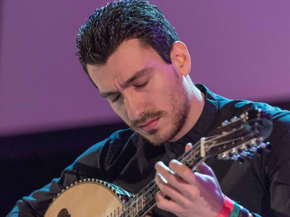 Vasilis Kostas playing the laouto on stage with a black shirt and his eyes closed