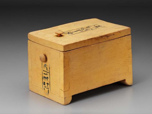 A small yellowish wooden box with buttons and inscriptions on the side and top.
