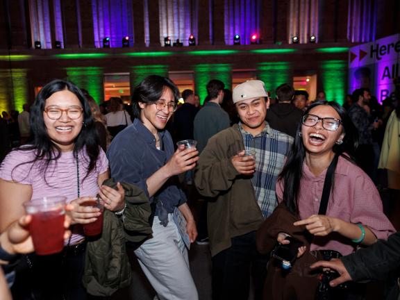 Young people smile and dance in a dark room with purple and green lights.