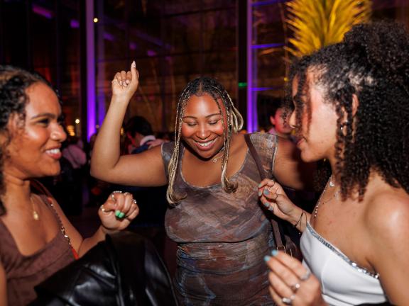 A group of young people smile and dance in a purple room.