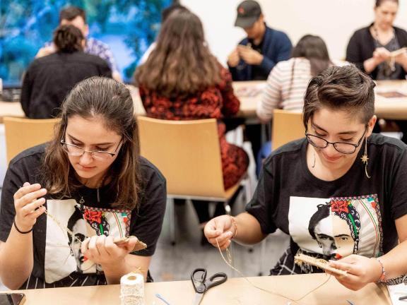 Two young people both wear t-shirts depicting Frida Kahlo and work on an art-making activity side by side 