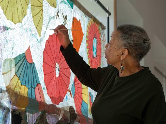 Artist Suzanne Jackson painting a red, green, and yellow abstract image.