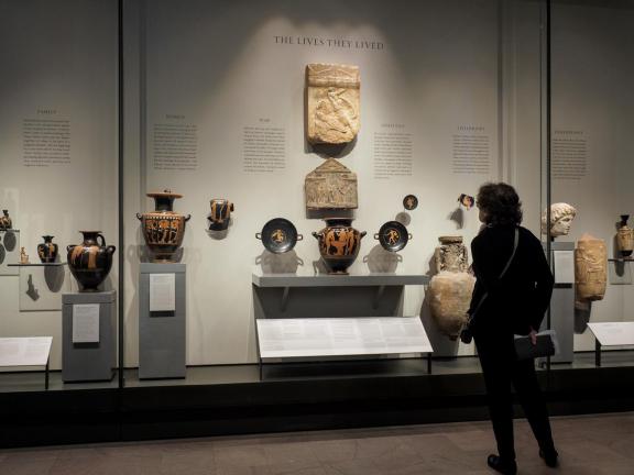 Visitor looking at display case filled with Ancient Greek pottery depicting scenes from daily life