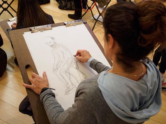 Woman sketching a bearded man sitting on large drawing pad