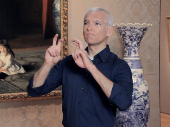 ASL interpreter signing in front of painting and vase