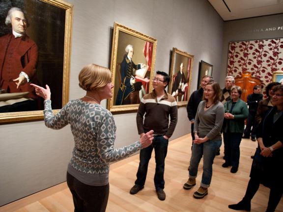 Guide pointing to Samuel Adams portrait with tour group in Revolutionary Boston gallery
