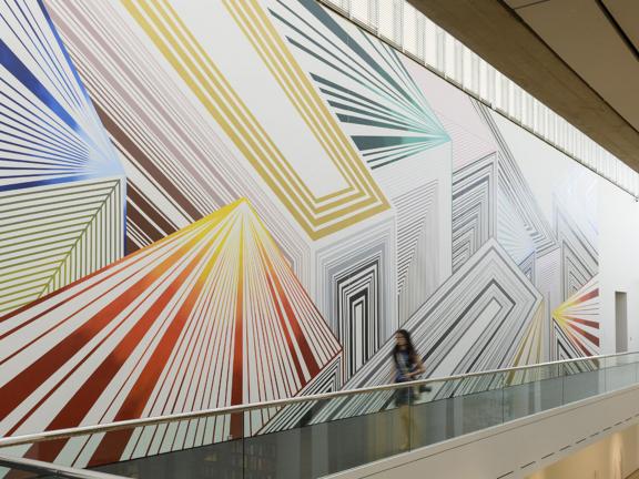 View of large mural, Tread Lightly, featuring angled geometric shapes, on wall in Linde Family Wing