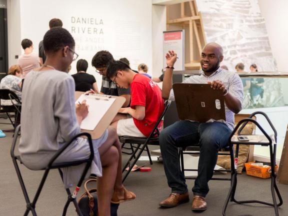 Visitors sitting on gallery stools drawing on second floor of Linde Family Wing